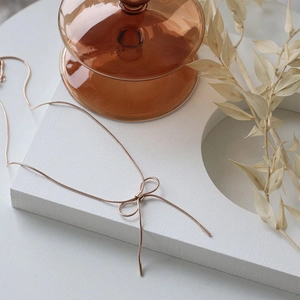 Elegant rose gold bow pendant on thin snake chain necklace displayed on white marble stone