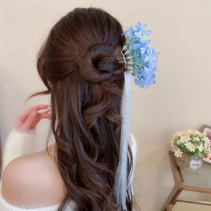 Detail of blue fabric flower hair pin with long translucent white ribbon on wavy hair