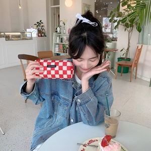 Detail showing red and white checkered corduroy pencil case held by a model in a cafe
