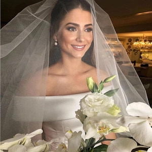 Elegant off-shoulder white satin wedding dress with a long layered tulle bridal veil