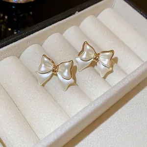 Elegant gold-plated bow earrings with cream resin inlay on a white velvet display tray
