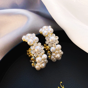 Detail of C-shaped gold-plated hoop earrings with pearls and rhinestone flower cluster
