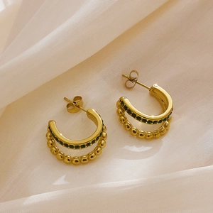 Detail of double-layer gold hoop earrings with green gemstones on silk background