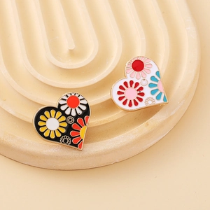 Detailed close-up of heart-shaped enamel flower brooches on a textured beige base