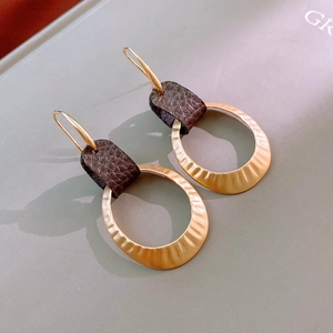 Detail of gold hammered metal hoop earrings with dark brown leather buckle and hook