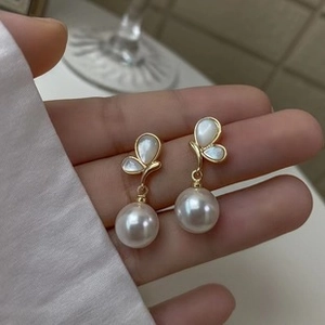 Detailed close-up of gold butterfly earrings with mother-of-pearl inlay and round pearl drop