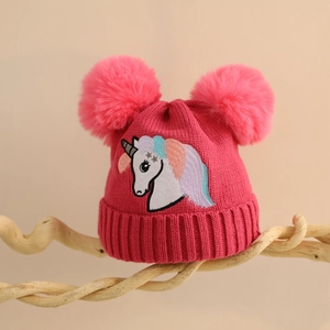 Detail der Kinder-Strickmütze in Rosa mit Bommeln und Einhorn-Stickerei auf Holzständer