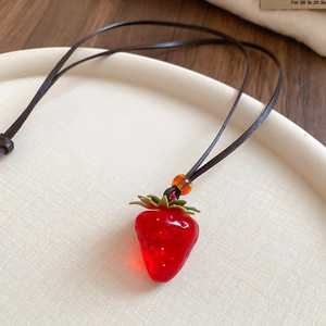 Detailed view of realistic red resin strawberry pendant on a dark brown leather cord