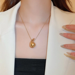 Close-up of minimalist gold teardrop pendant necklace worn by a model in a white blazer