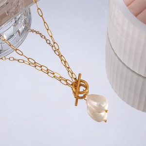 Macro view of gold chain necklace with baroque pearl and OT toggle clasp on blue surface