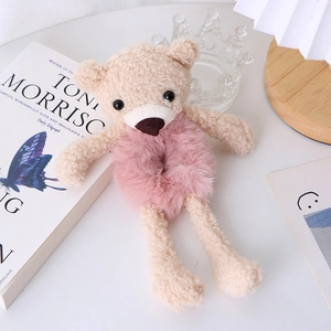 Detail view of a cute beige plush bear hair tie with soft pink velvet band on wooden desk