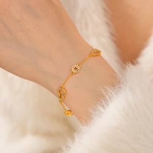 Macro detail of 24k gold-plated bracelet with zircon heart and coin charms on wrist
