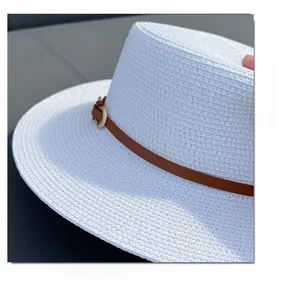 Detailed close-up of white straw hat with brown leather band and gold buckle detail