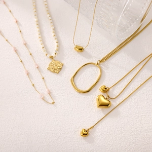 Chic layered gold necklaces featuring heart pendants and pink beads on white surface