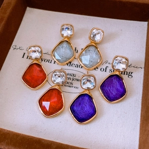 Close-up of geometric resin drop earrings in red purple and blue with gold finish
