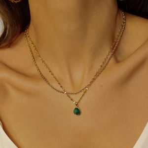 Detail of layered gold necklace featuring a pear-shaped green stone pendant on model