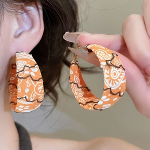 Détail de boucles d'oreilles créoles en tissu orange avec motif soleil et style ethnique