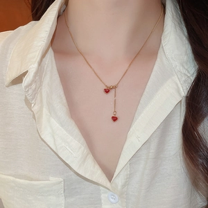 Detail of red heart pendant Y-necklace in gold finish worn by a model on white shirt