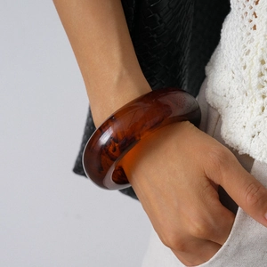 Detail shot of a thick amber resin bangle on wrist with stylish vintage contrast outfit