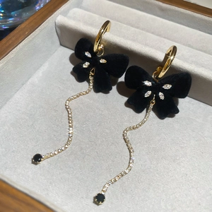 Close-up of black velvet bow earrings with rhinestone gold tassels in a jewelry box