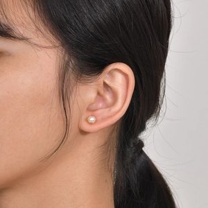 Close-up of a 6mm round white pearl stud earring with golden claw setting on an ear