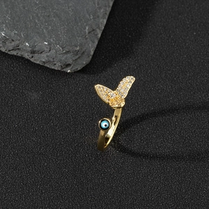 Detailed close-up of golden open ring with zircon butterfly and evil eye bead