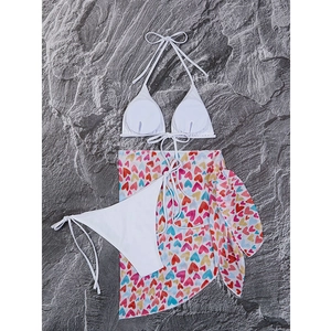 Flat lay of three-piece white bikini set with colorful heart print mesh beach sarong