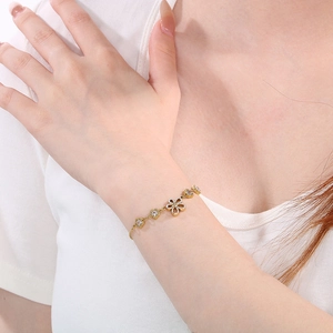 Detail of gold-tone bracelet with zircon flower and geometric charms on a model wrist