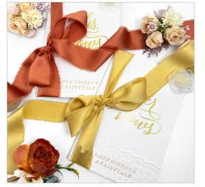 Macro detail of white wedding vow books with frayed silk ribbons and gold foil lettering