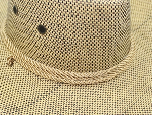 Detail of woven straw cowboy hat with gold decorative rope and metal ventilation eyelet