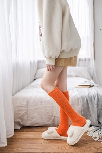 Close-up of warm orange coral fleece knee-high socks worn with white plush slippers