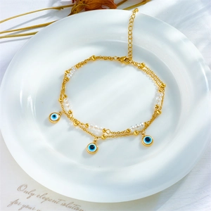 Layered gold evil eye anklet with turquoise beads and charms on white ceramic plate
