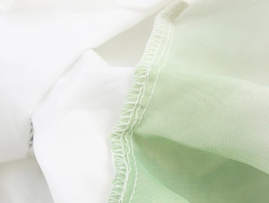 Detail view of reinforced edge stitching on green and white pleated chiffon fabric
