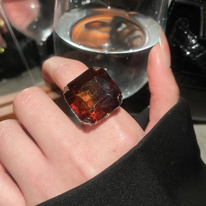 Macro detail of a large square orange-red amber resin ring with silver four-claw setting