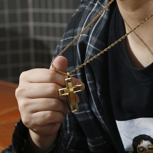 Detail of a golden double-layered hollow cross pendant with twist chain worn by a male model