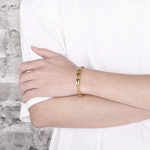 Gros plan d'un bracelet doré à maillons en H au poignet sur un fond neutre texturé