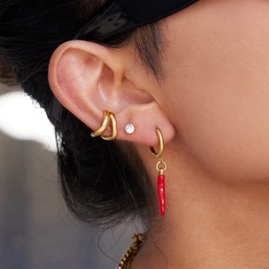 Close-up of gold ear cuff, diamond stud, and hoop earring with red chili pendant detail