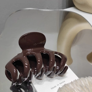 Detail of a dark brown glossy hair claw clip on a minimalist wavy mirror surface