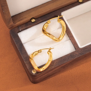 Golden irregular twisted stainless steel hoop earrings on a luxury wooden jewelry box