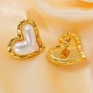 Detailed close-up of golden heart earrings with hammered texture and pearl inlay