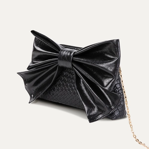 Detail view of black textured leather bag with oversized bow and golden metal chain