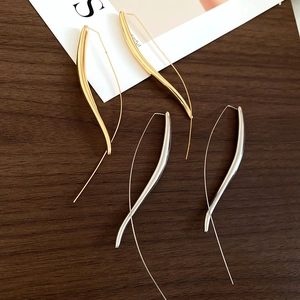 Detail of minimalist gold and silver teardrop earrings on a dark wood background