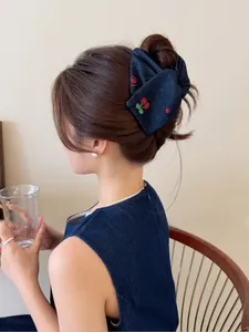 Détail d'une pince à cheveux en jean avec broderies de cerises sur un chignon élégant