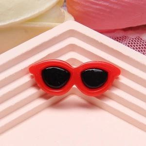 Macro shot of small red heart-shaped resin sunglasses on a pink geometric stand
