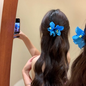 Dettaglio ravvicinato di un fermaglio a fiore blu vibrante su folti capelli ondulati