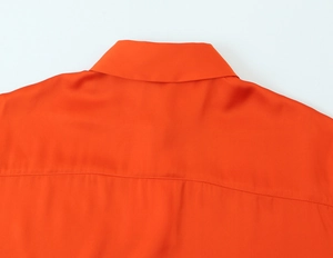 Detailed close-up of the orange satin shirt collar and shoulder with smooth silk texture