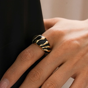 Macro shot of a black enamel wide ring with irregular gold wave textures on finger
