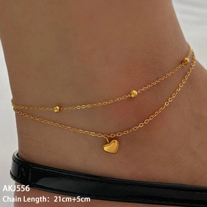 Close-up of double-layer gold anklet with heart pendant and beads worn on ankle