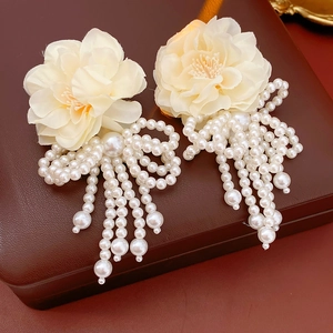 Detail of floral earrings with white faux pearl tassels and bows on a brown background