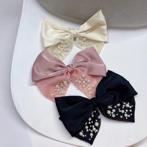 Dettaglio di tre fermagli a fiocco in crema, rosa e nero con perle sintetiche applicate